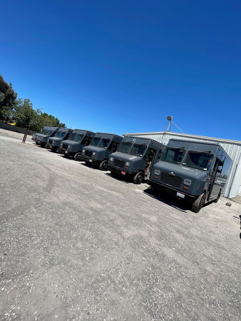 Row of six gray delivery step vans in a fleet yard