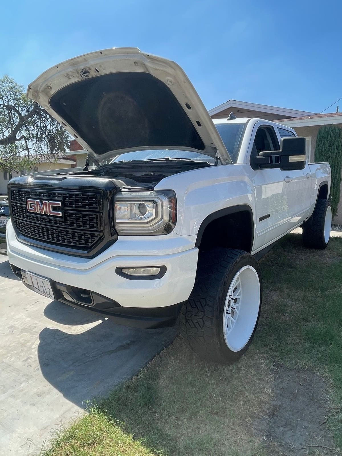 White GMC Sierra pickup with the hood open in a residential driveway